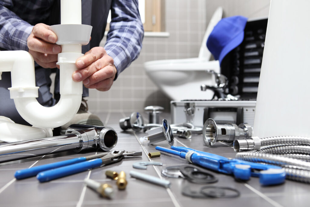 Plumber installing bathroom waste pipe with tools and fittings during plumbing repair work.