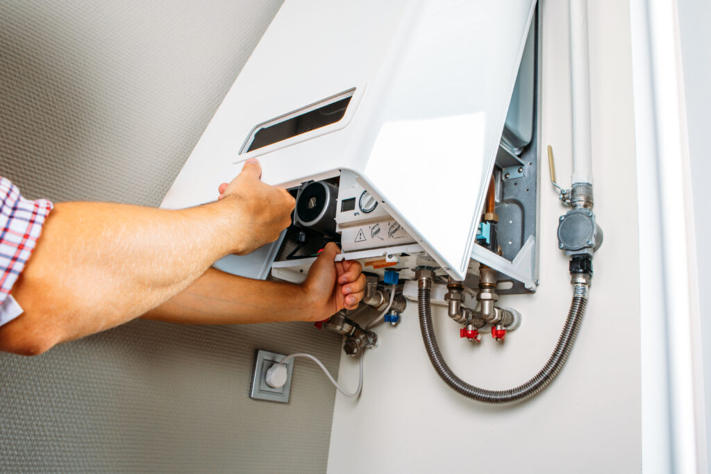 Heating engineer servicing a wall-mounted boiler, checking internal components and pipe connections.