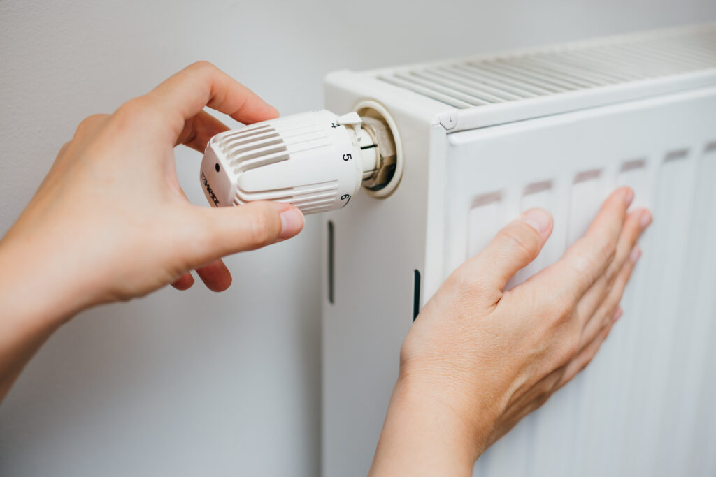 Hand adjusting a radiator thermostat valve to control home heating temperature.