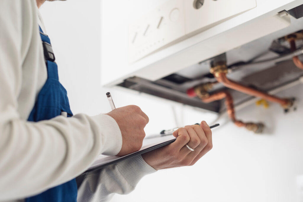 Heating engineer inspecting a wall-mounted boiler and taking notes during routine servicing.